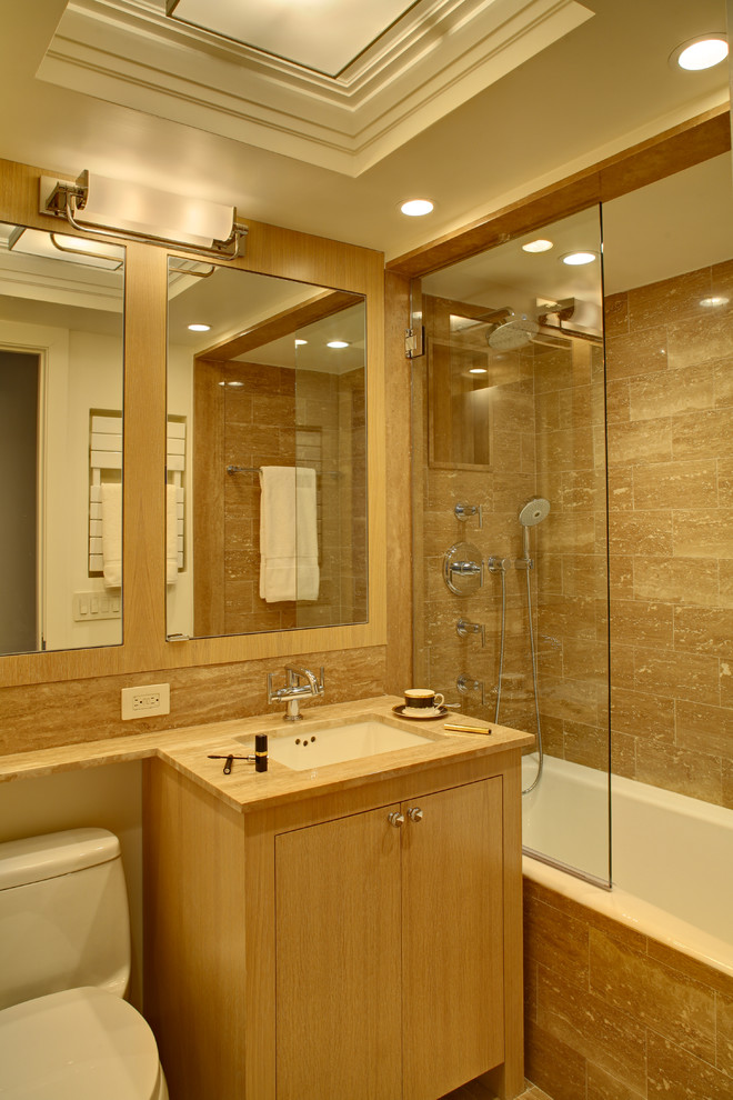 ニューヨークにある小さなトランジショナルスタイルのおしゃれな浴室 (フラットパネル扉のキャビネット、淡色木目調キャビネット、ドロップイン型浴槽、シャワー付き浴槽	、分離型トイレ、ベージュのタイル、セラミックタイル、ベージュの壁、アンダーカウンター洗面器) の写真