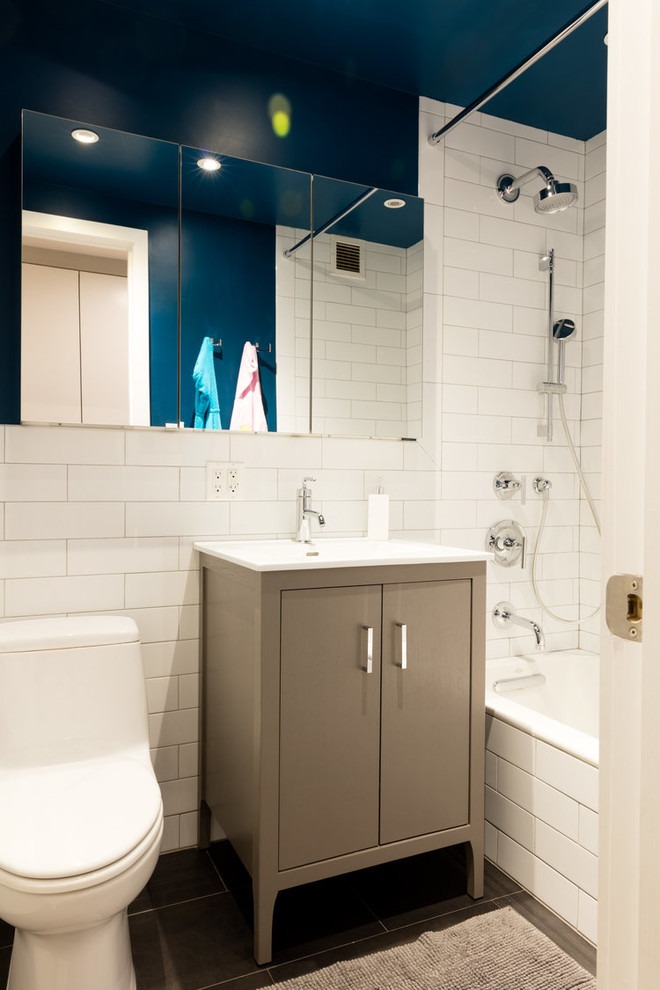 This is an example of a medium sized contemporary shower room bathroom in New York with flat-panel cabinets, beige cabinets, an alcove bath, a shower/bath combination, a one-piece toilet, white tiles, metro tiles, blue walls, porcelain flooring, an integrated sink, engineered stone worktops, grey floors and a shower curtain.