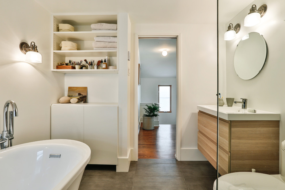 Idéer för att renovera ett funkis badrum, med ett integrerad handfat, släta luckor, skåp i ljust trä, ett fristående badkar, en toalettstol med separat cisternkåpa och vita väggar