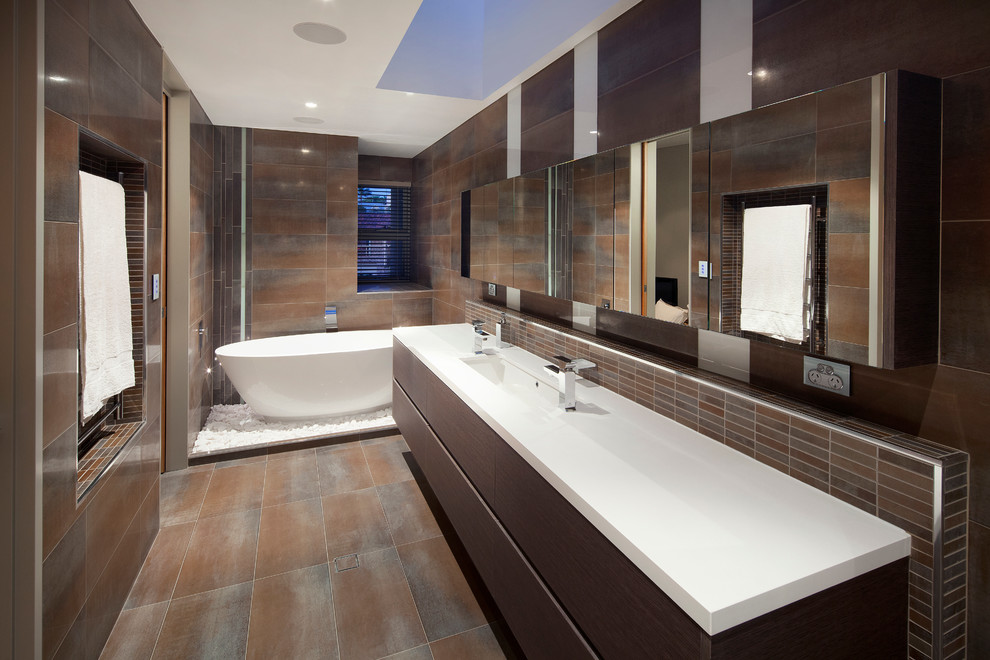 Идея дизайна: большая, узкая и длинная ванная комната в современном стиле с отдельно стоящей ванной, монолитной раковиной, плоскими фасадами, темными деревянными фасадами, столешницей из искусственного кварца, коричневой плиткой, коричневыми стенами и полом из керамической плитки