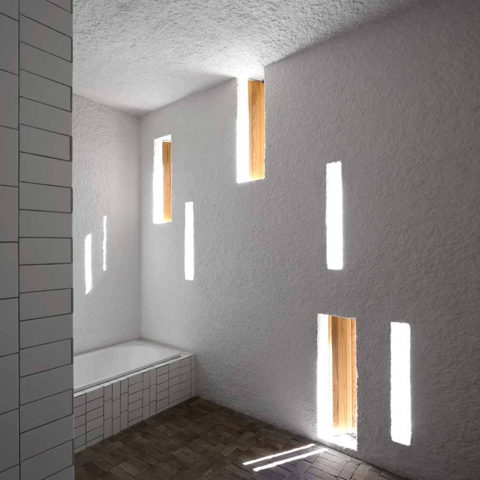 Ispirazione per una stanza da bagno design con vasca da incasso, piastrelle bianche, piastrelle in gres porcellanato, pareti bianche e pavimento in mattoni