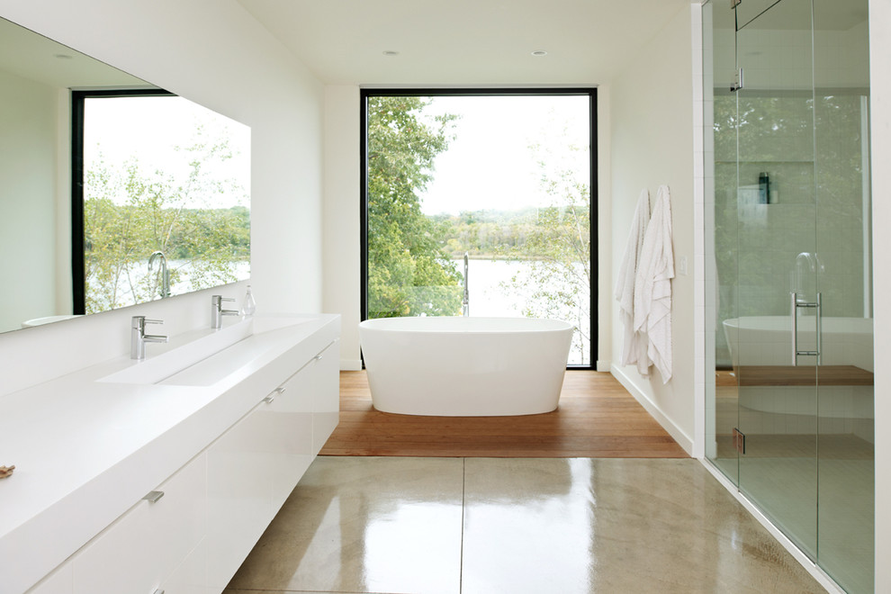 Inredning av ett modernt mellanstort en-suite badrum, med ett avlångt handfat, släta luckor, vita skåp, ett fristående badkar, en dusch i en alkov, vit kakel, betonggolv och vita väggar