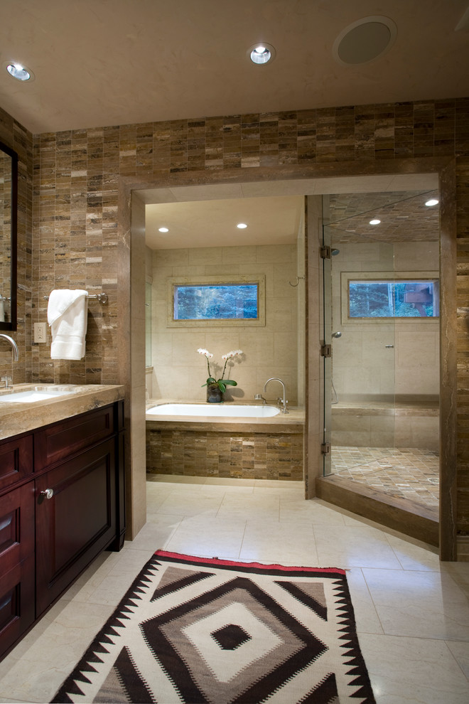 Example of a mid-sized trendy master beige tile and stone tile ceramic tile corner shower design in Denver with raised-panel cabinets, dark wood cabinets, an undermount tub, beige walls, an undermount sink and granite countertops
