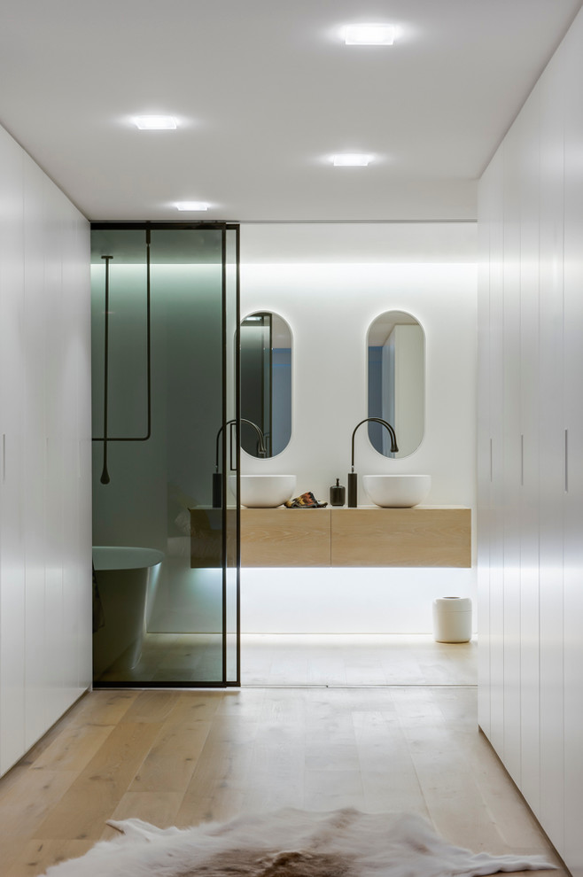 Cette image montre une douche en alcôve principale design en bois clair de taille moyenne avec une vasque, un placard à porte plane, un plan de toilette en bois, une baignoire indépendante, un carrelage blanc, un mur blanc et parquet clair.