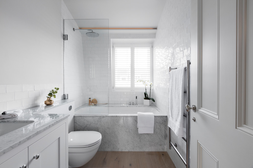 Cette image montre une salle de bain nordique avec un placard à porte shaker, des portes de placard blanches, un combiné douche/baignoire, WC à poser, un carrelage métro, un mur blanc, parquet clair, un sol beige et aucune cabine.