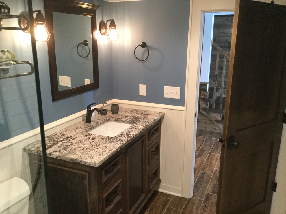 Cette image montre une salle de bain craftsman en bois foncé de taille moyenne avec un placard avec porte à panneau encastré, WC séparés, un mur bleu, un sol en vinyl, un lavabo encastré, un sol marron, une cabine de douche à porte battante, un carrelage blanc, un carrelage métro, un plan de toilette en granite et un plan de toilette beige.