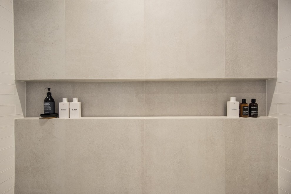 Modelo de cuarto de baño principal actual con ducha doble, baldosas y/o azulejos blancos, baldosas y/o azulejos de cemento, paredes blancas, lavabo sobreencimera, encimera de mármol, sanitario de pared, suelo de baldosas de porcelana y suelo gris
