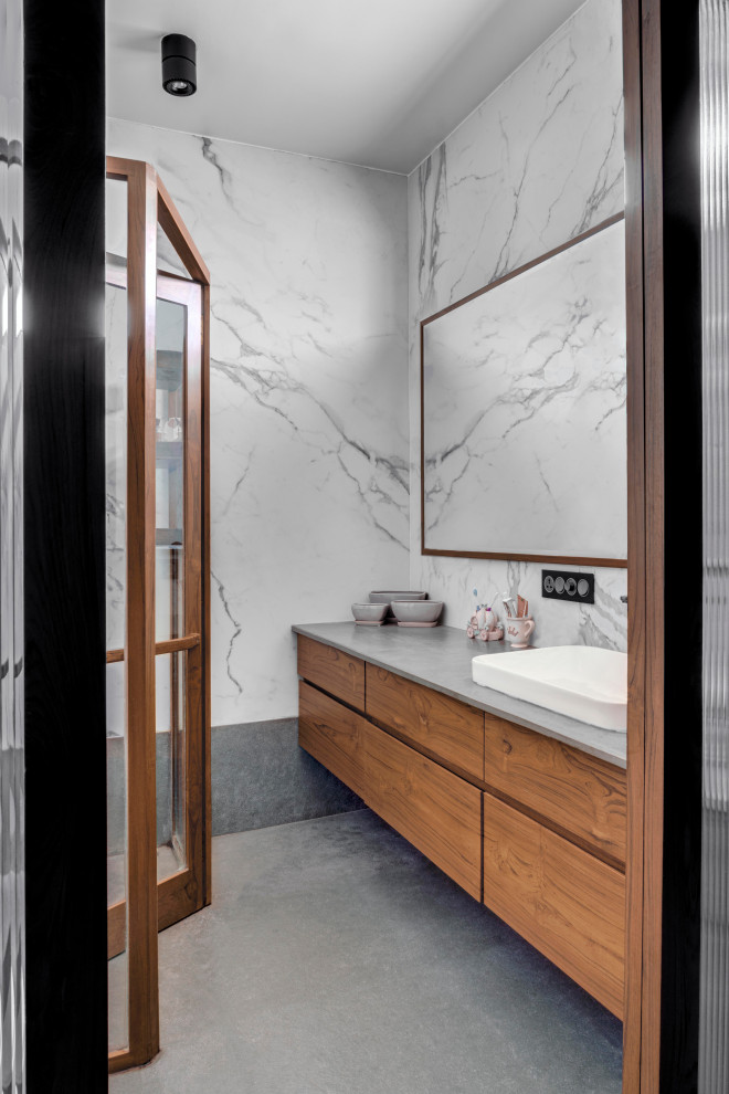 Modernes Badezimmer mit flächenbündigen Schrankfronten, hellbraunen Holzschränken, weißer Wandfarbe, Aufsatzwaschbecken, grauem Boden, grauer Waschtischplatte und Einzelwaschbecken in Pune