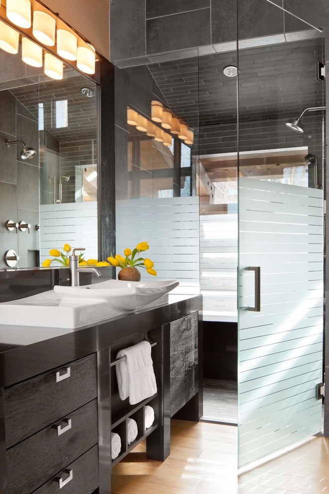 Réalisation d'une salle de bain design avec une vasque, des portes de placard noires, un plan de toilette en quartz, une douche à l'italienne, un carrelage gris, des carreaux de porcelaine et un placard à porte plane.