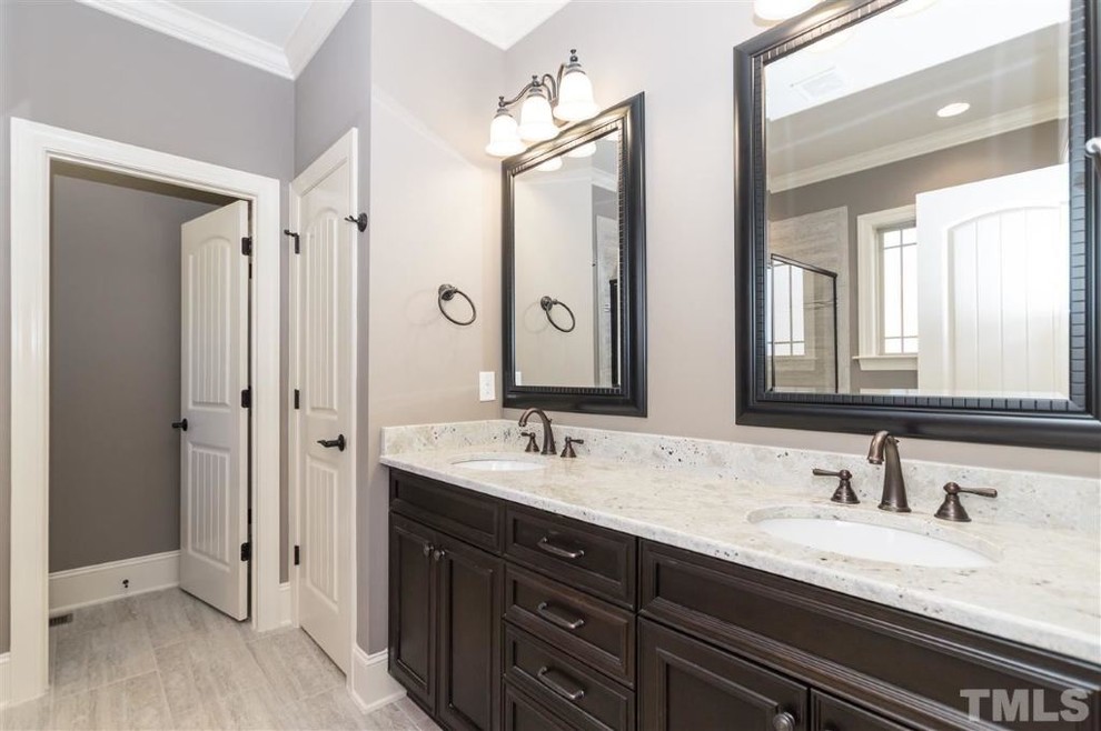Inspiration for a large traditional ensuite bathroom in Raleigh with a submerged sink, flat-panel cabinets, dark wood cabinets, granite worktops, an alcove shower, a one-piece toilet, grey tiles, ceramic tiles, grey walls and ceramic flooring.