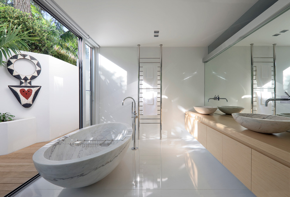 Exempel på ett mellanstort modernt beige beige badrum, med ett fristående handfat, släta luckor, skåp i ljust trä, träbänkskiva, ett fristående badkar och vita väggar