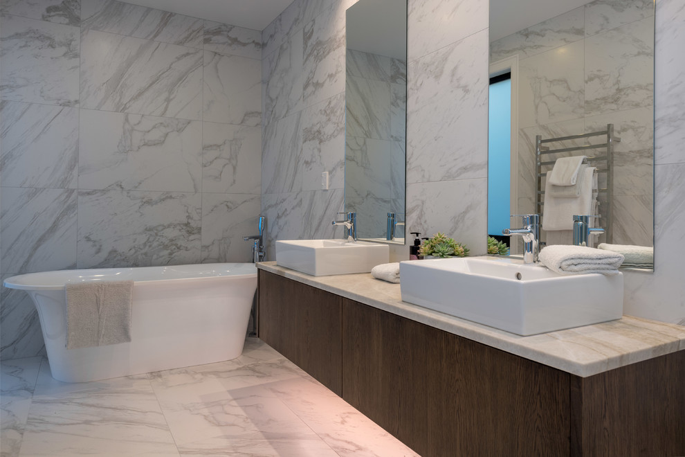 Design ideas for a medium sized contemporary ensuite bathroom in Auckland with medium wood cabinets, a freestanding bath, grey tiles, porcelain tiles, grey walls, porcelain flooring, a vessel sink, grey floors, flat-panel cabinets and tiled worktops.