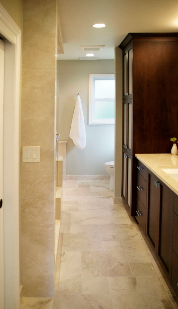 Esempio di una stanza da bagno padronale classica con ante in legno bruno, vasca ad angolo, doccia aperta, WC monopezzo, pareti beige, lavabo da incasso e top in pietra calcarea