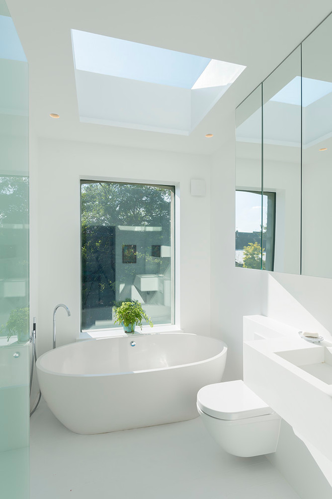 Modelo de cuarto de baño principal actual con lavabo integrado, bañera exenta, paredes blancas y sanitario de pared