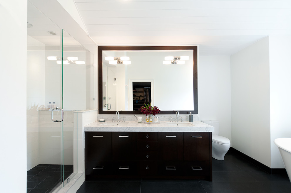 На фото: ванная комната в современном стиле с врезной раковиной, плоскими фасадами, темными деревянными фасадами, мраморной столешницей, отдельно стоящей ванной и душем в нише с