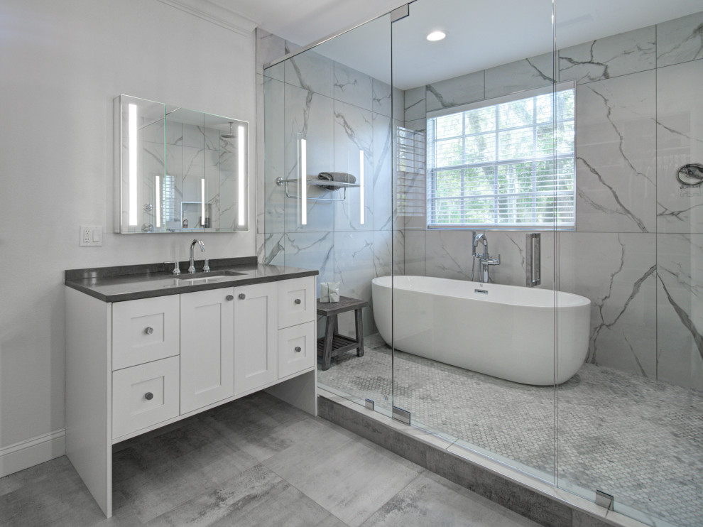 Foto på ett stort funkis grå en-suite badrum, med luckor med infälld panel, vita skåp, ett fristående badkar, en dusch/badkar-kombination, vit kakel, porslinskakel, vita väggar, klinkergolv i porslin, ett undermonterad handfat, bänkskiva i kvarts, grått golv och dusch med gångjärnsdörr