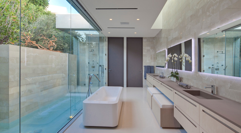 Diseño de cuarto de baño contemporáneo con lavabo integrado, armarios con paneles lisos, puertas de armario de madera clara, bañera exenta, baldosas y/o azulejos grises y encimeras grises