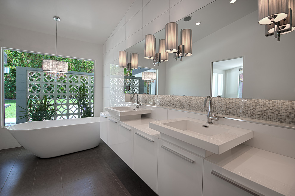 Bild på ett 60 tals badrum, med ett fristående handfat, släta luckor, vita skåp, ett fristående badkar, grå kakel och mosaik