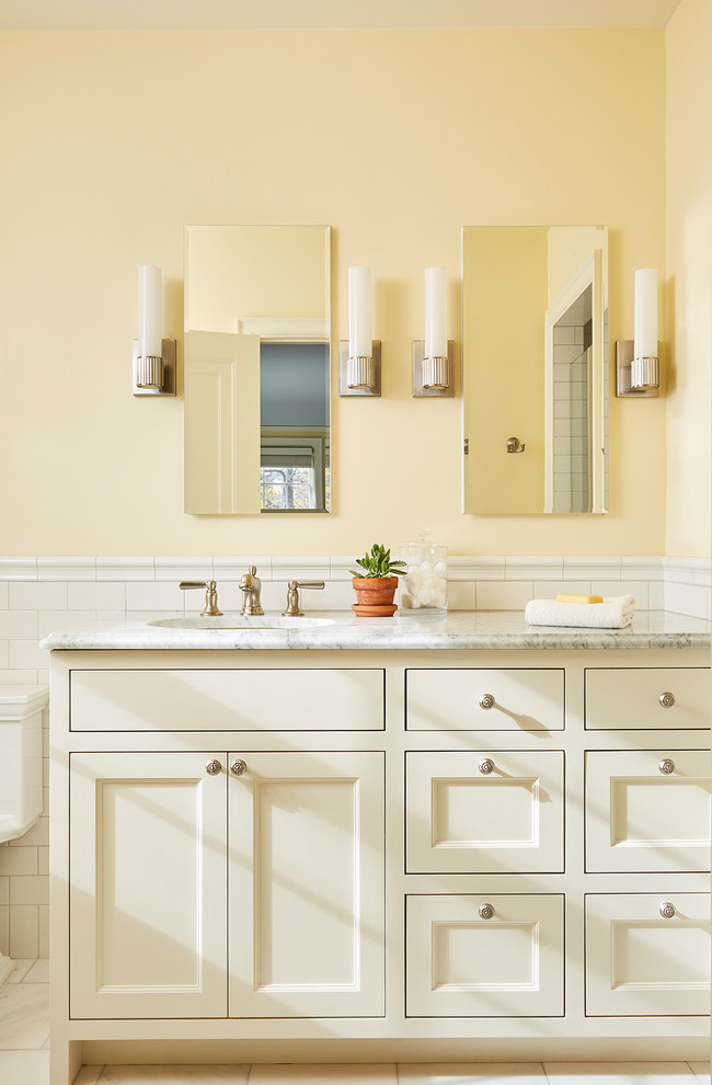 Exemple d'une salle de bain chic avec un placard avec porte à panneau encastré, des portes de placard beiges, un carrelage blanc, un carrelage métro, un mur jaune, un lavabo encastré, un plan de toilette gris et un plan de toilette en marbre.