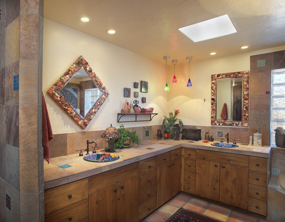 Inredning av ett eklektiskt badrum, med ett nedsänkt handfat, skåp i slitet trä, kaklad bänkskiva, ett hörnbadkar, perrakottakakel, beige väggar, klinkergolv i terrakotta och brun kakel
