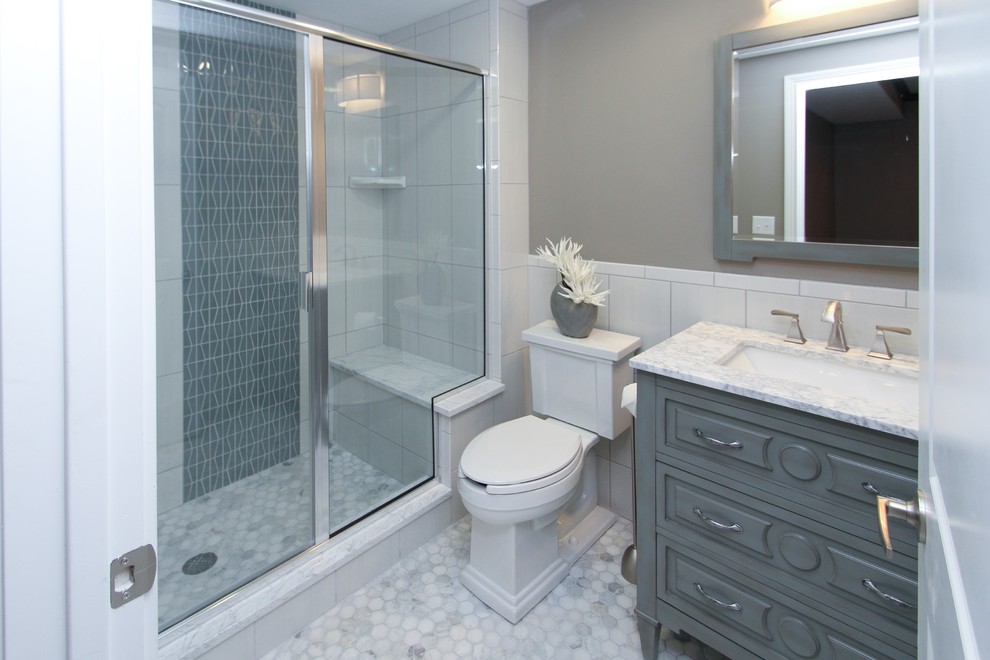 Klassisk inredning av ett mellanstort badrum med dusch, med möbel-liknande, grå skåp, en dusch i en alkov, en toalettstol med separat cisternkåpa, vit kakel, keramikplattor, grå väggar, klinkergolv i keramik, ett undermonterad handfat och marmorbänkskiva