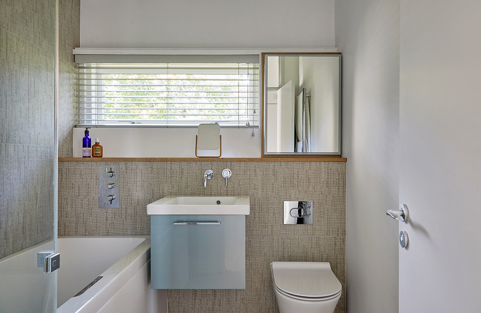 Kleines Mid-Century Badezimmer mit flächenbündigen Schrankfronten, blauen Schränken, Duschbadewanne, Wandtoilette und Wandwaschbecken in Surrey
