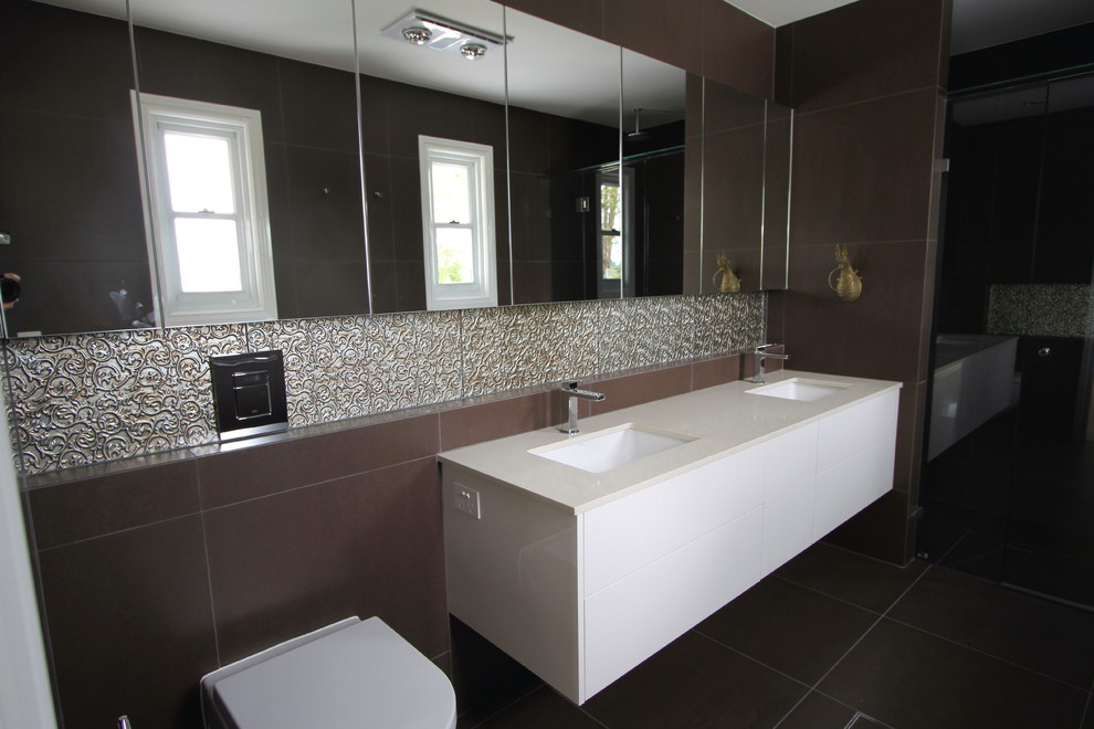 Inspiration för mellanstora moderna en-suite badrum, med ett undermonterad handfat, släta luckor, vita skåp, bänkskiva i kvarts, en vägghängd toalettstol, brun kakel, porslinskakel, bruna väggar och klinkergolv i porslin