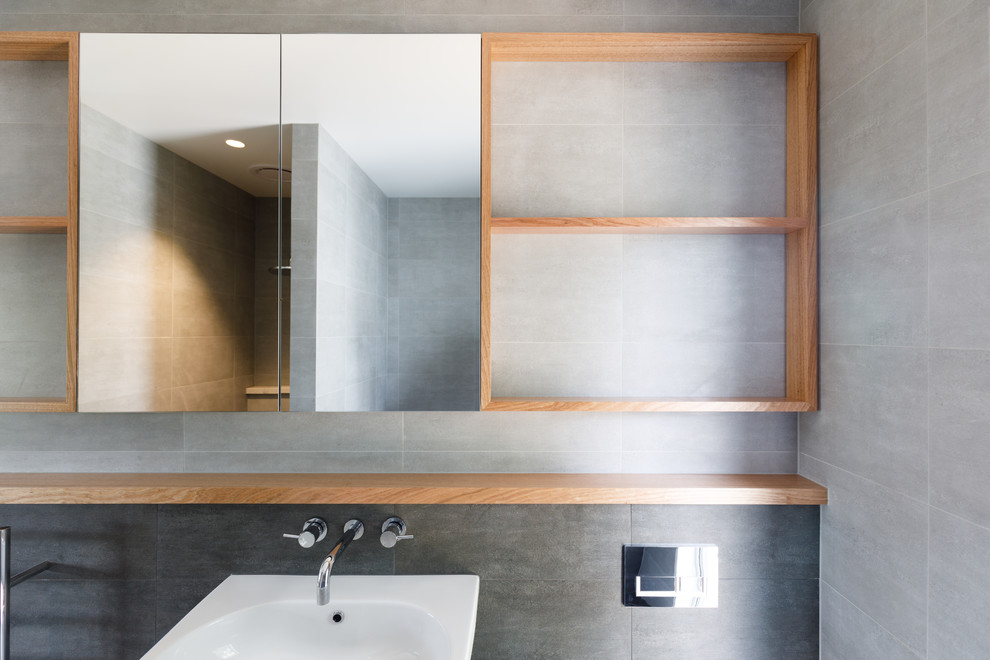Inspiration for a medium sized contemporary shower room bathroom in Hobart with flat-panel cabinets, a built-in bath, an alcove shower, a wall mounted toilet, grey tiles, ceramic tiles, grey walls, ceramic flooring, a wall-mounted sink and tiled worktops.