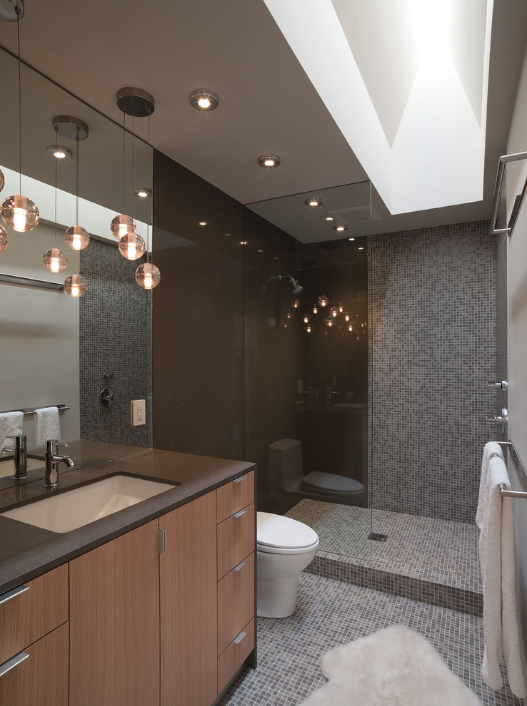 Small trendy mosaic tile and gray tile mosaic tile floor and gray floor bathroom photo in Austin with an undermount sink, gray walls, medium tone wood cabinets, solid surface countertops, a one-piece toilet, flat-panel cabinets and brown countertops