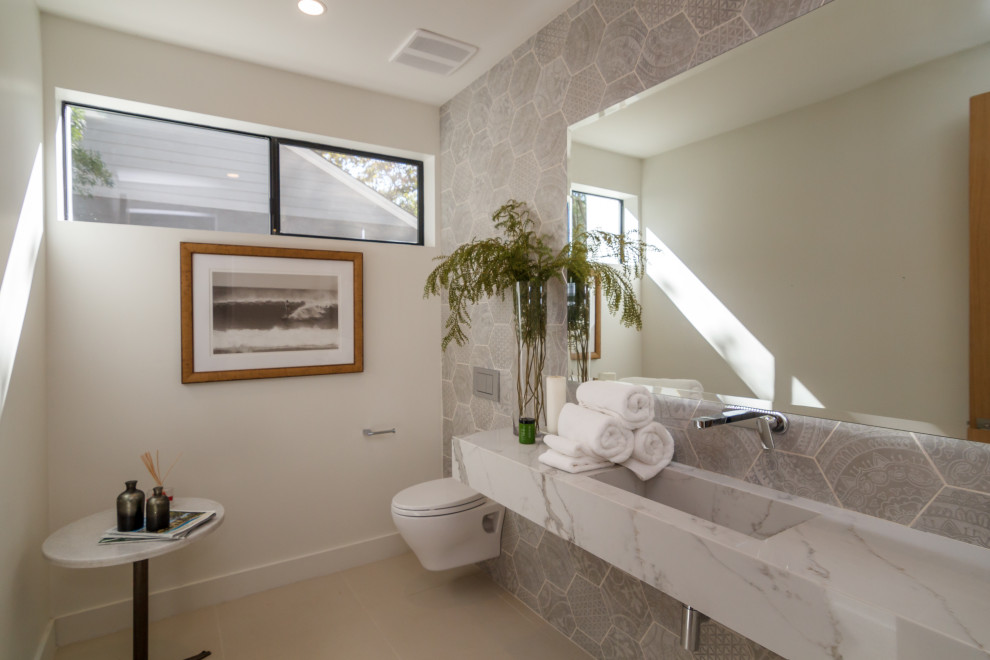 Immagine di una stanza da bagno minimal con WC sospeso, piastrelle grigie, pareti bianche, lavabo integrato, pavimento beige, top bianco e un lavabo