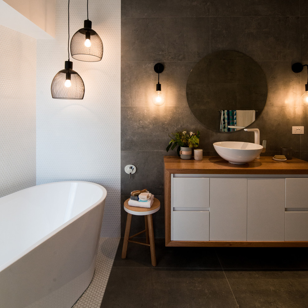 Modelo de cuarto de baño actual con bañera exenta, baldosas y/o azulejos blancos, paredes grises y lavabo sobreencimera