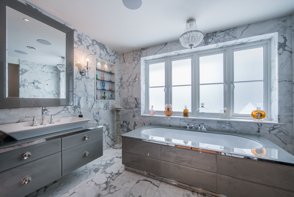 Contemporary ensuite bathroom in London with flat-panel cabinets, grey cabinets, a built-in bath, grey tiles, marble tiles, grey walls, marble flooring, a vessel sink, glass worktops and grey floors.
