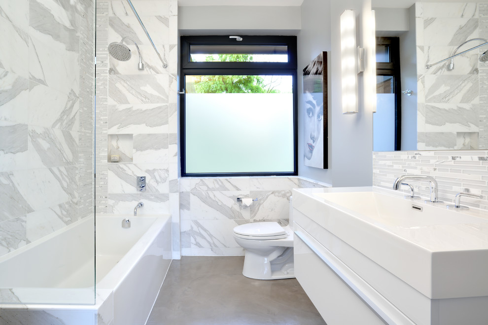 Пример оригинального дизайна: ванная комната в современном стиле с раковиной с несколькими смесителями, плоскими фасадами, белыми фасадами, ванной в нише, душем в нише, раздельным унитазом, серой плиткой, бетонным полом и столешницей из кварцита