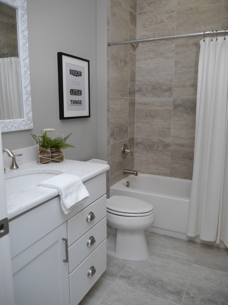 Amerikansk inredning av ett stort vit vitt badrum med dusch, med släta luckor, vita skåp, ett badkar i en alkov, en dusch i en alkov, en toalettstol med separat cisternkåpa, grå kakel, kakelplattor, grå väggar, cementgolv, ett nedsänkt handfat, laminatbänkskiva, grått golv och dusch med duschdraperi