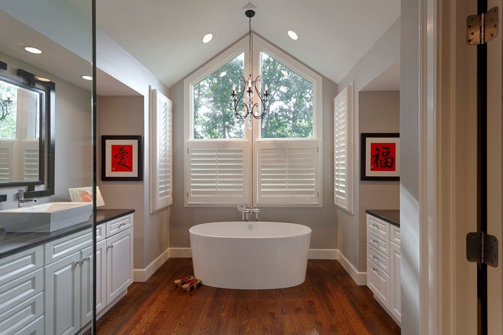 Foto på ett mellanstort vintage en-suite badrum, med luckor med upphöjd panel, vita skåp, ett fristående badkar, grå väggar, mörkt trägolv, ett fristående handfat, bänkskiva i akrylsten och brunt golv