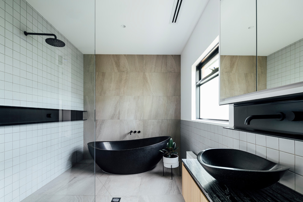 Inspiration for a contemporary bathroom in Melbourne with a freestanding bath, a built-in shower, grey tiles, a vessel sink, grey floors, black worktops, flat-panel cabinets and light wood cabinets.