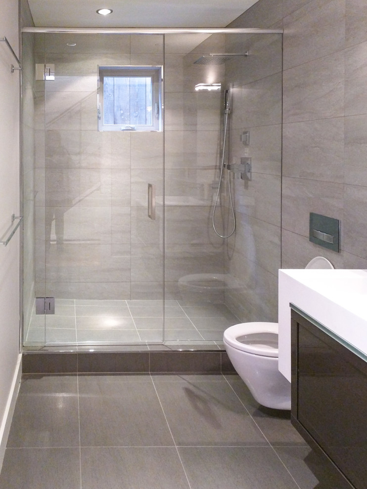 Diseño de cuarto de baño contemporáneo de tamaño medio con armarios con paneles lisos, puertas de armario de madera oscura, sanitario de pared, baldosas y/o azulejos grises, lavabo integrado y encimera de cuarzo compacto