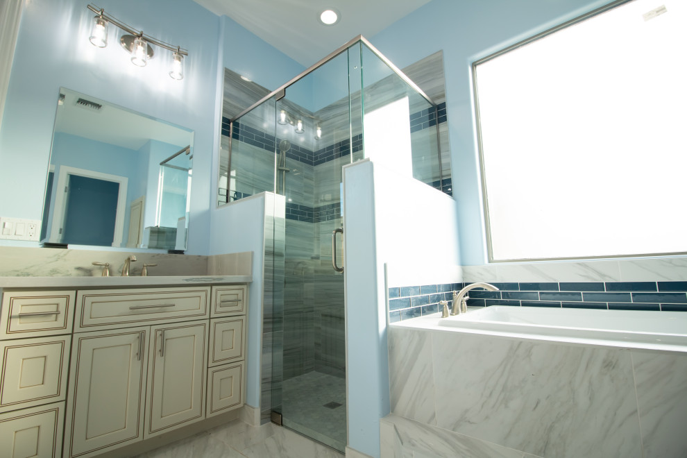 Exemple d'une grande salle de bain principale tendance avec un placard à porte affleurante, des portes de placard beiges, une baignoire posée, une douche d'angle, WC séparés, un carrelage bleu, un carrelage métro, un mur bleu, un sol en marbre, un lavabo encastré, un plan de toilette en marbre, un sol gris, une cabine de douche à porte battante et un plan de toilette blanc.