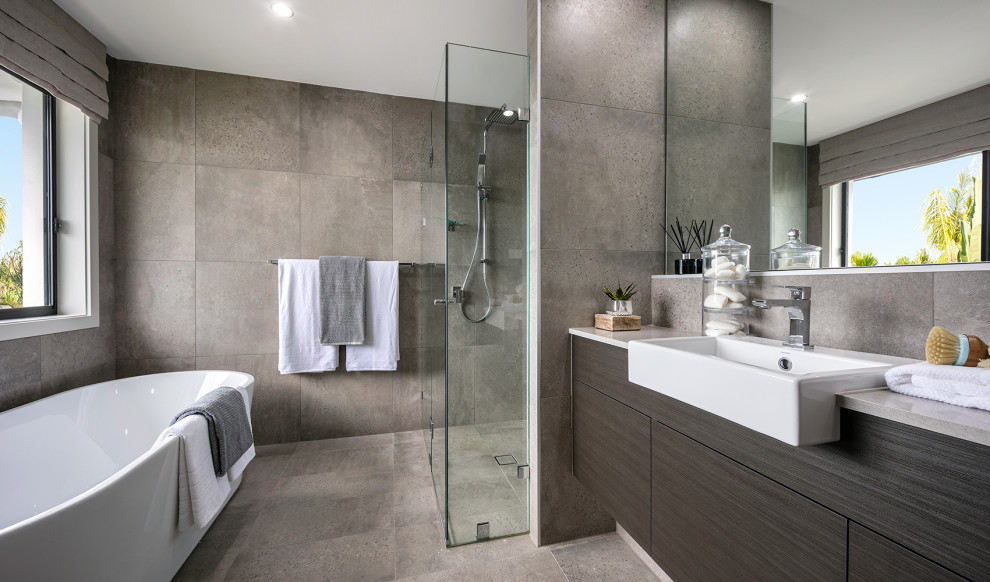 Inredning av ett modernt mellanstort grå grått en-suite badrum, med släta luckor, skåp i mörkt trä, ett fristående badkar, en kantlös dusch, grå kakel, ett fristående handfat, grått golv och dusch med gångjärnsdörr