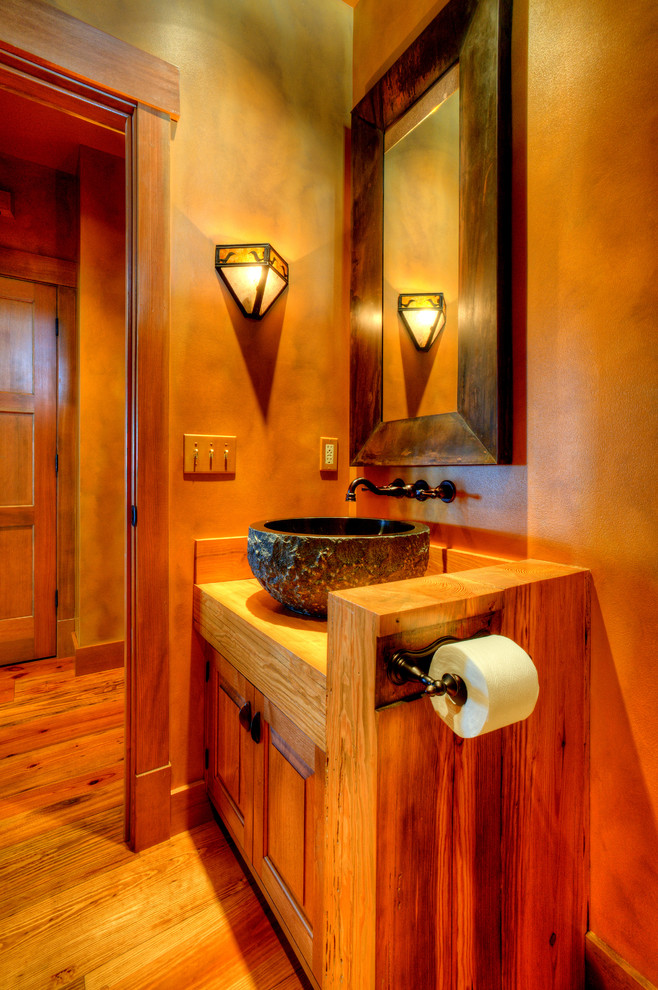 Aménagement d'une salle d'eau campagne en bois brun de taille moyenne avec un placard avec porte à panneau surélevé, WC à poser, un mur beige, un sol en bois brun, une vasque, un plan de toilette en bois, un sol marron et un plan de toilette marron.