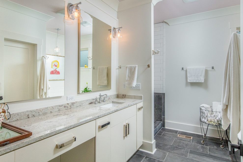 Klassisk inredning av ett badrum, med släta luckor, vita skåp, en dusch i en alkov, vit kakel, vita väggar, ett undermonterad handfat, grått golv och med dusch som är öppen