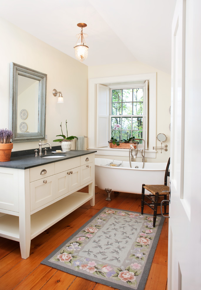 Réalisation d'une salle de bain champêtre avec un placard à porte shaker, des portes de placard beiges, une baignoire sur pieds, un mur beige, un sol en bois brun et un lavabo encastré.