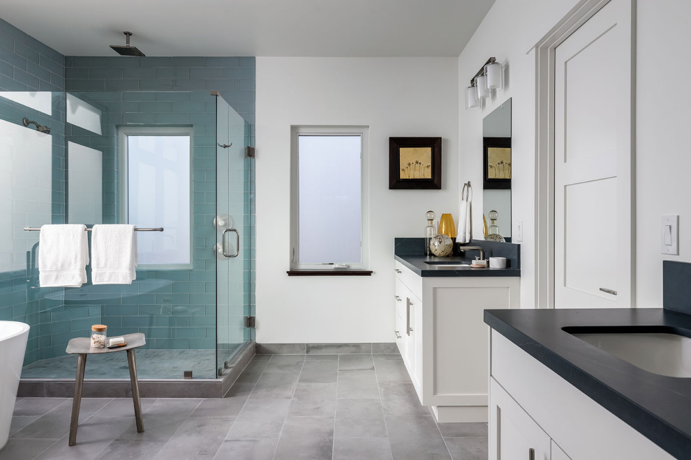 Cette image montre une grande salle de bain principale traditionnelle avec un placard à porte shaker, des portes de placard blanches, une baignoire indépendante, une douche d'angle, WC à poser, un carrelage bleu, un carrelage en pâte de verre, un mur blanc, un sol en carrelage de porcelaine, un lavabo encastré, un plan de toilette en quartz modifié, un sol gris, une cabine de douche à porte battante et un plan de toilette noir.