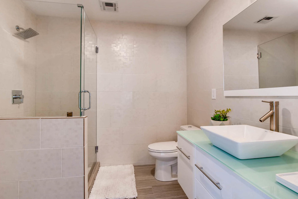 На фото: ванная комната в современном стиле с плоскими фасадами, белыми фасадами, угловым душем, раздельным унитазом, бежевой плиткой, бежевыми стенами, душевой кабиной, настольной раковиной, стеклянной столешницей, душем с распашными дверями и зеленой столешницей с
