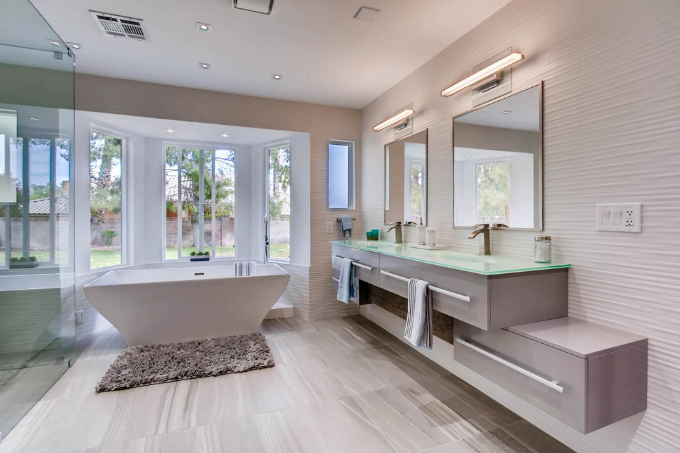 Modernes Badezimmer En Suite mit flächenbündigen Schrankfronten, grauen Schränken, freistehender Badewanne, Eckdusche, weißen Fliesen, beiger Wandfarbe, integriertem Waschbecken, Glaswaschbecken/Glaswaschtisch, grauem Boden und Falttür-Duschabtrennung in Las Vegas