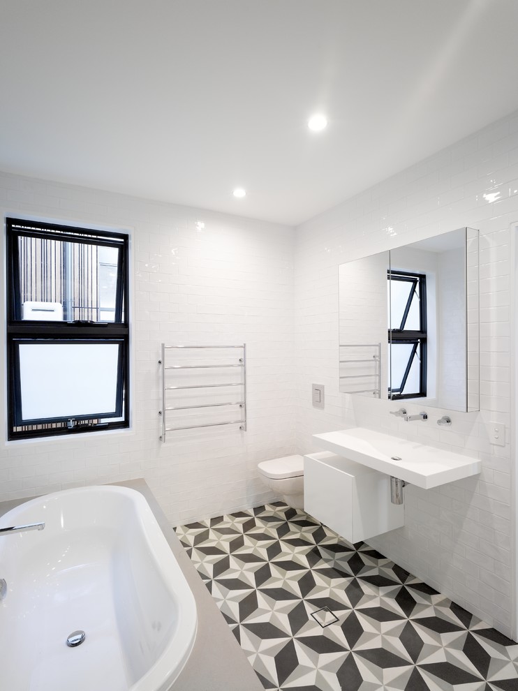 Design ideas for a contemporary bathroom in Sydney with flat-panel cabinets, white cabinets, a corner bath, a wall mounted toilet, white tiles, metro tiles, white walls, ceramic flooring and a wall-mounted sink.