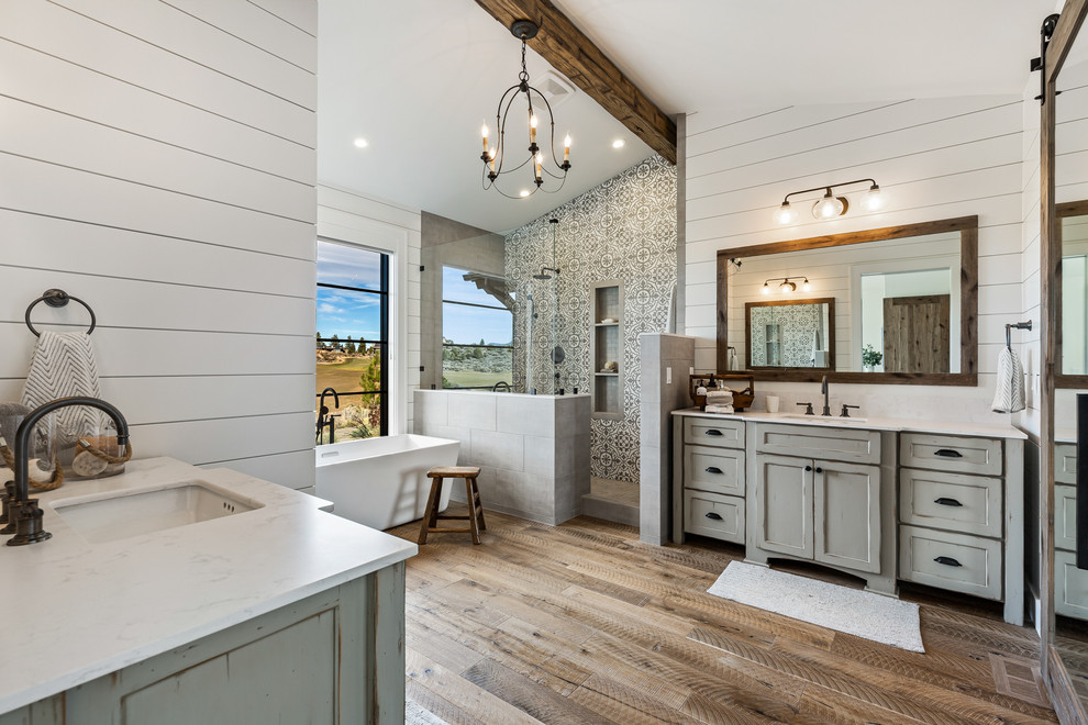 Lantlig inredning av ett mellanstort grå grått en-suite badrum, med grå skåp, en öppen dusch, vit kakel, cementkakel, vita väggar, mellanmörkt trägolv, ett undermonterad handfat, bänkskiva i kvarts, brunt golv, med dusch som är öppen och luckor med infälld panel