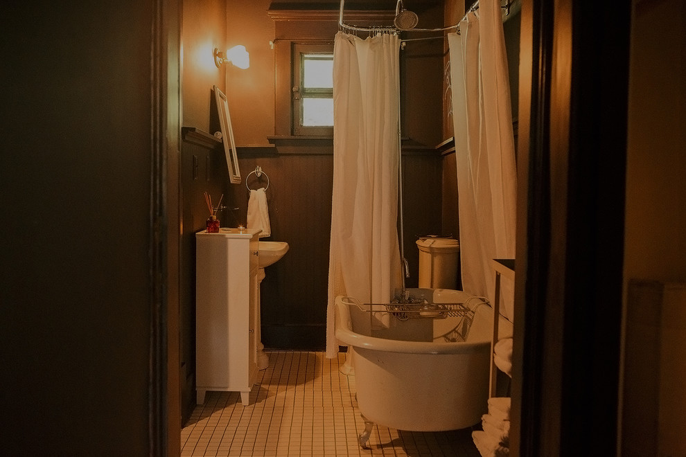 На фото: ванная комната в белых тонах с отделкой деревом: освещение в стиле модернизм с фасадами в стиле шейкер, белыми фасадами, ванной на ножках, душем над ванной, унитазом-моноблоком, фиолетовыми стенами, темным паркетным полом, раковиной с пьедесталом, мраморной столешницей, коричневым полом, шторкой для ванной, белой столешницей, тумбой под одну раковину, напольной тумбой, сводчатым потолком и панелями на части стены с