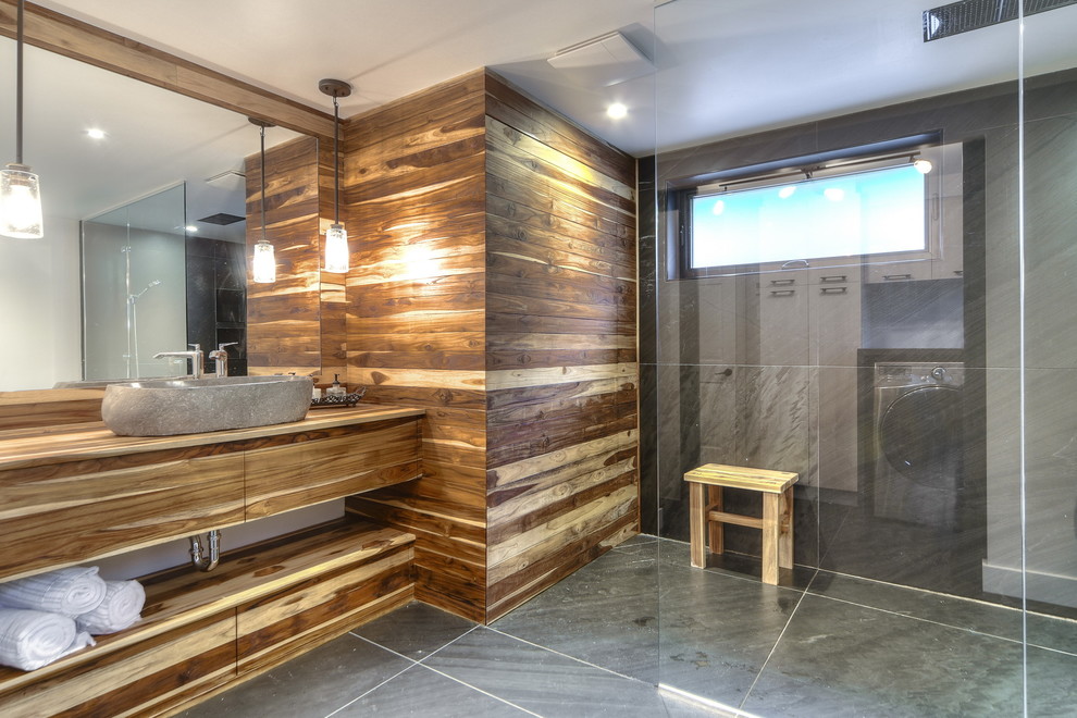 На фото: большая главная ванная комната в стиле фьюжн с плоскими фасадами, светлыми деревянными фасадами, открытым душем, унитазом-моноблоком, черной плиткой, каменной плиткой, серыми стенами, полом из сланца и столешницей из дерева