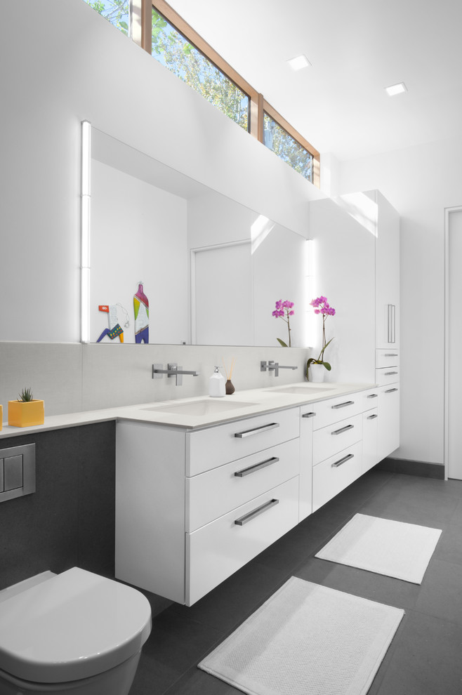 Inredning av ett 50 tals en-suite badrum, med släta luckor, vita skåp, en vägghängd toalettstol, vita väggar, betonggolv, ett undermonterad handfat och grått golv